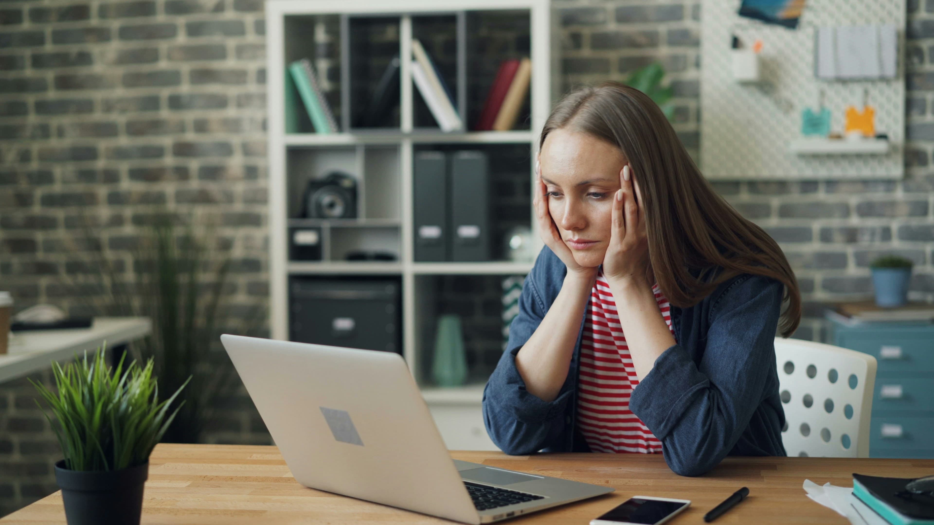 Woman working at desk with laptop, experiencing focus challenges - representing the struggle with phone distraction